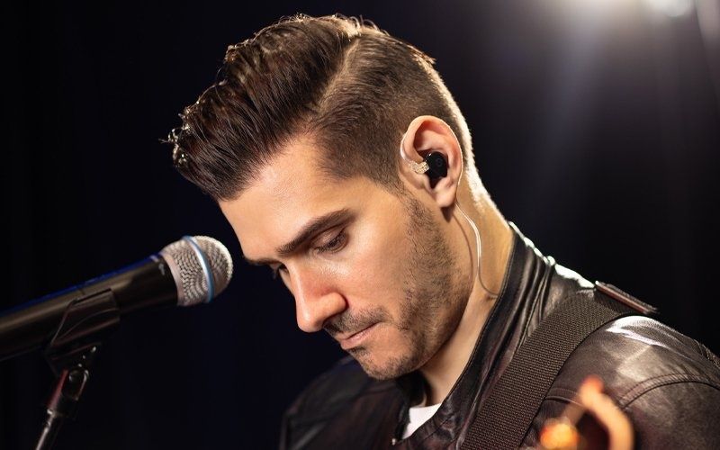 Musiker mit In-Ear-Monitor am Mikrofon auf einer dunklen Bühne